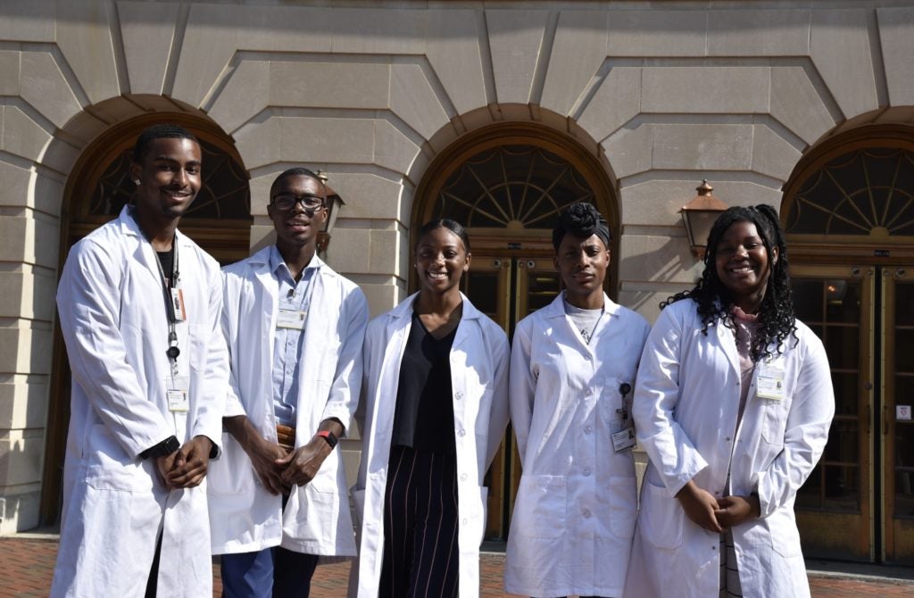 Five students in white coats outside Med-Dent
