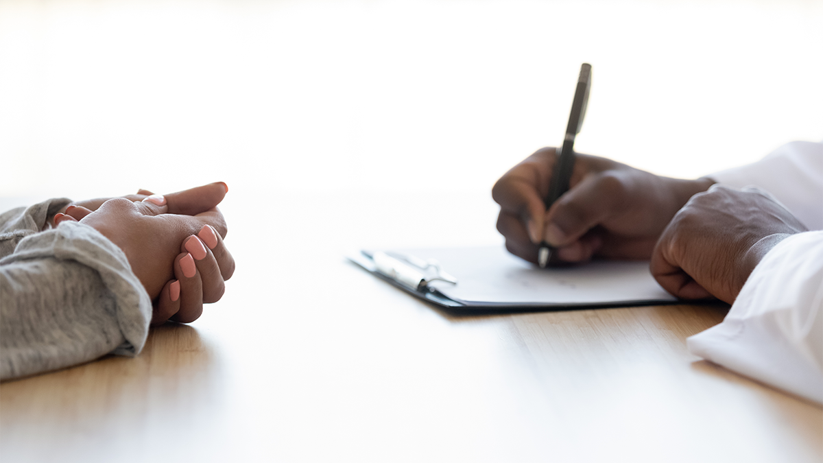 Two sets of hands, one clasped, the other writing on a clipboard with a pen
