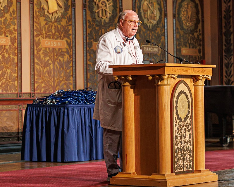Dr. Mitchell speaks from a podium onstage in Gaston Hall