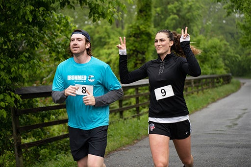 Two IronMed runners run together, one raises her arms and flashes a peace sign