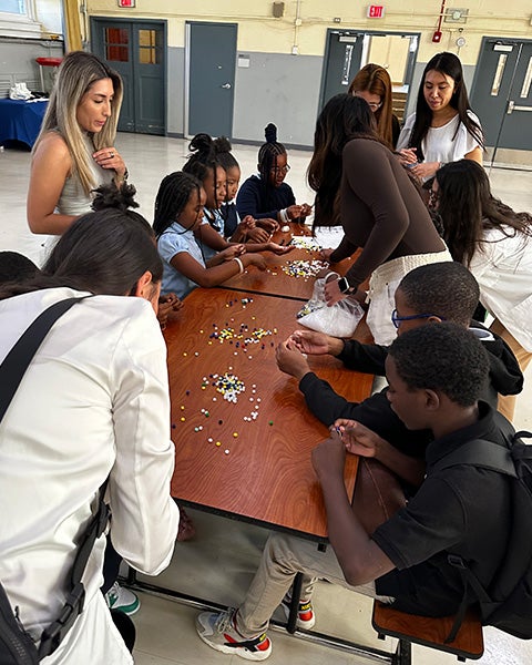 Students sit at a table and string beads onto cords