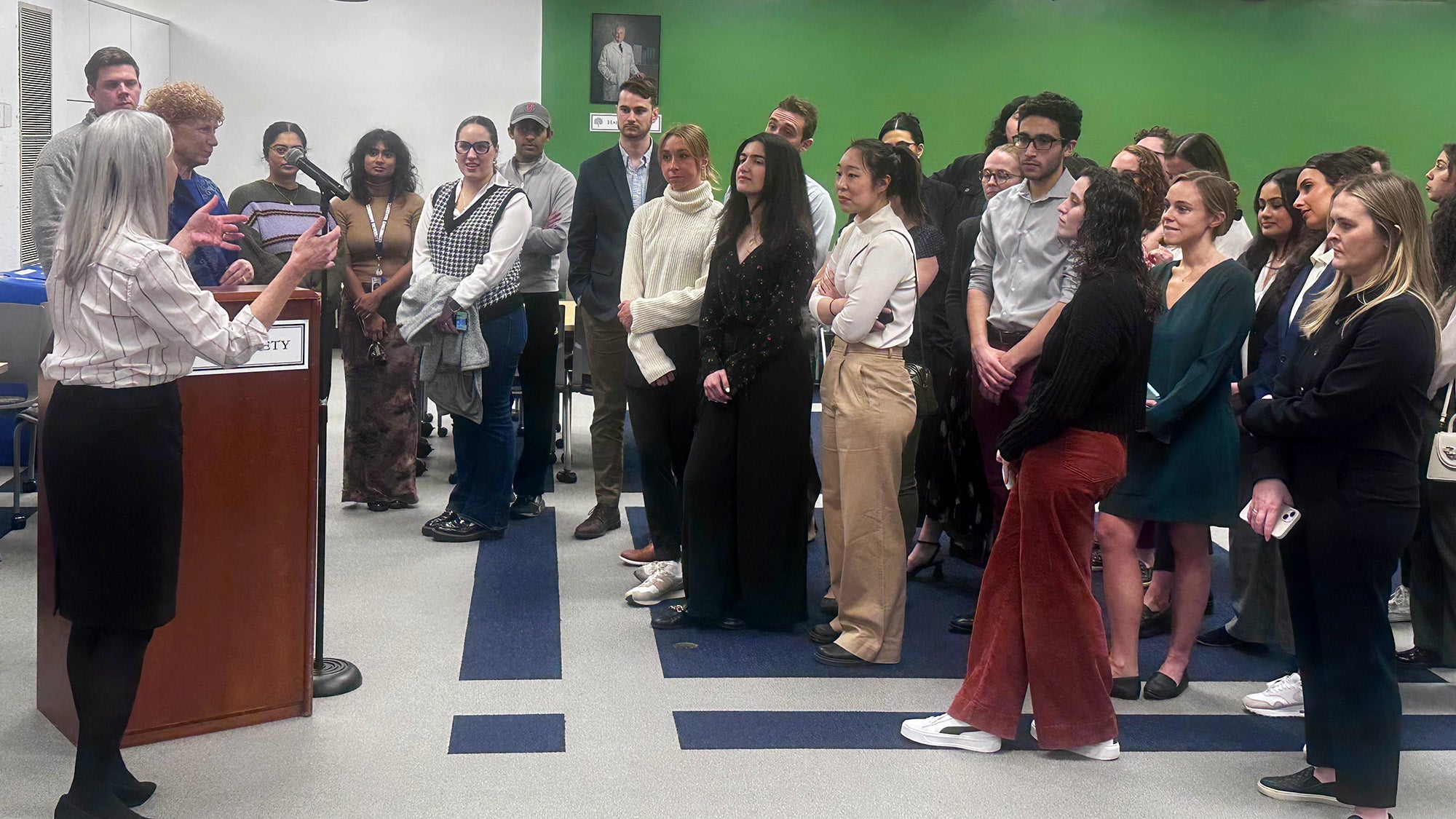 A group of students stands together and listens as Dr. Girard and Dr. Moore speak to them