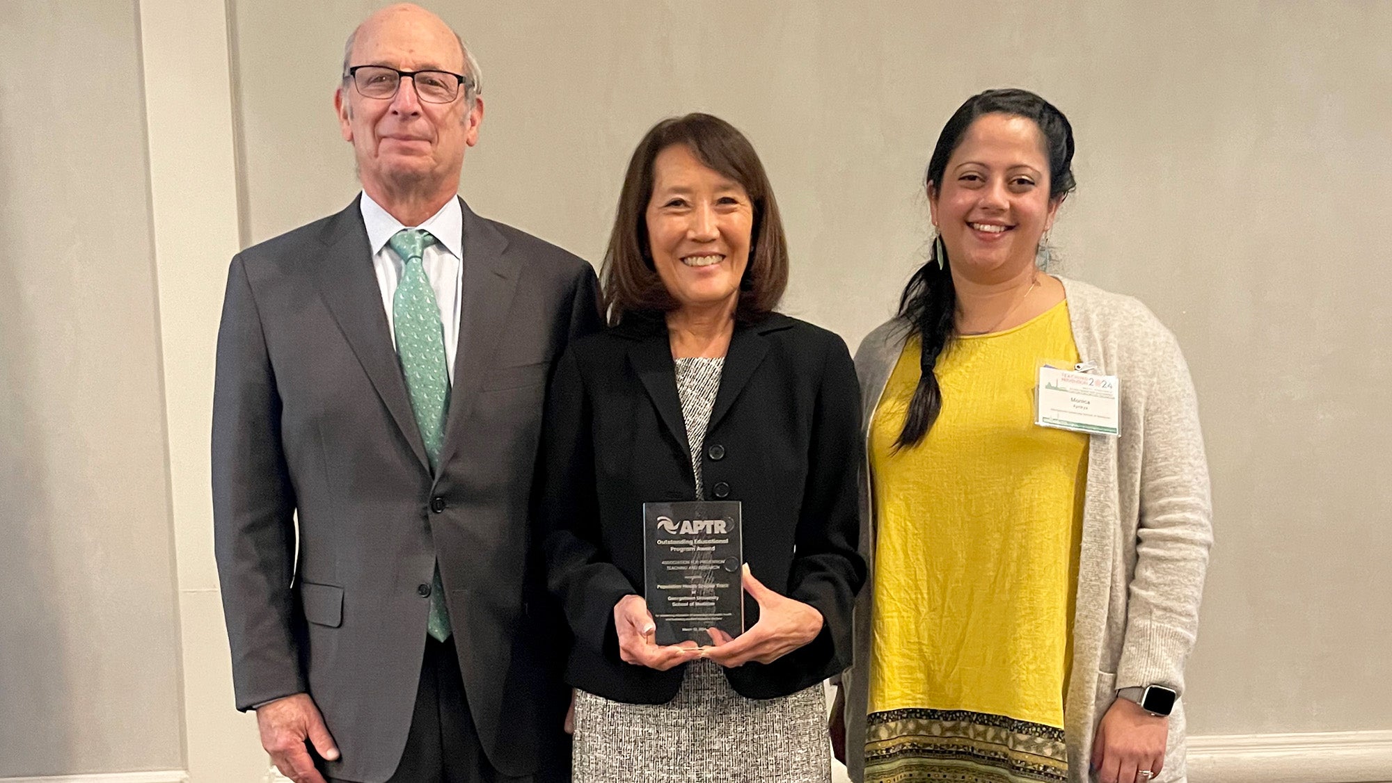 Three individuals stand together, one holding an award