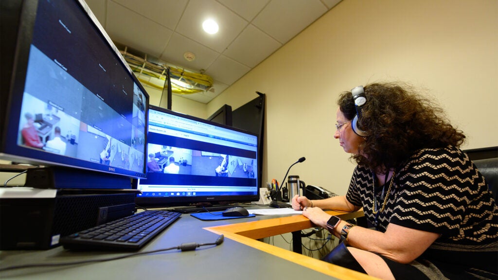 A faculty members monitors the ILC learning spaces on video screens in front of her and through headphones she is wearing