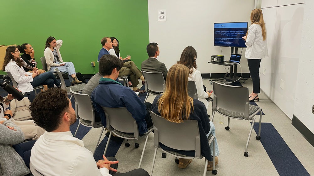 A medical student presents her research to fellow students and faculty members
