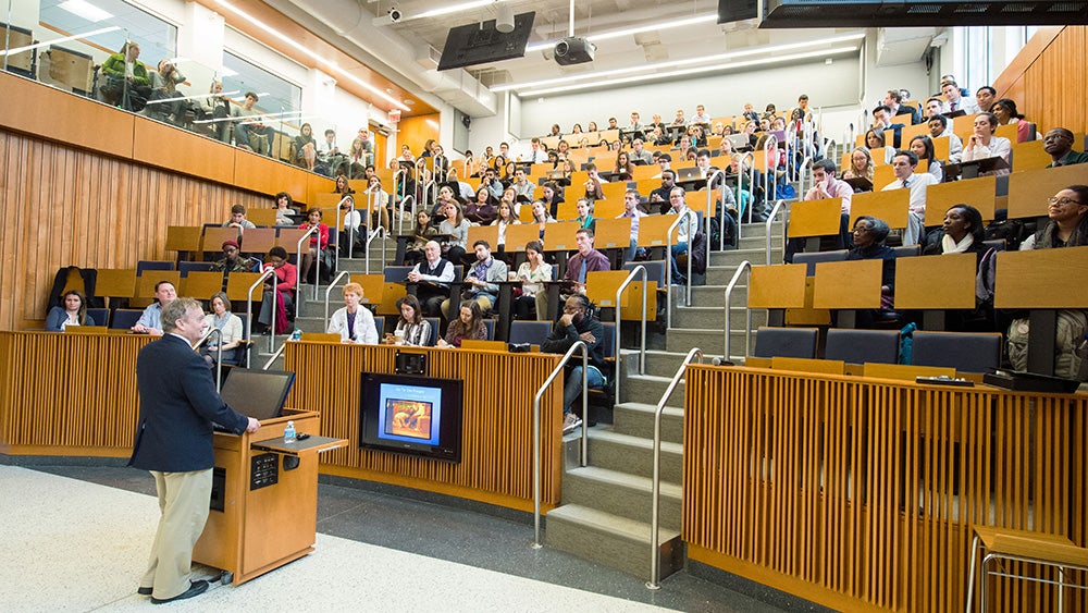 People sit in chairs in Proctor Harvey Amphitheater while a speaker addresses them from a podium on the floor