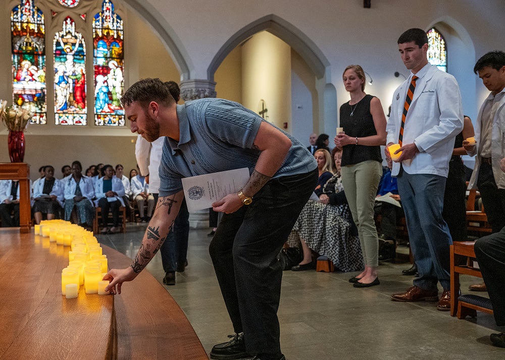A man sets a lit candle on the step in front of the altar in Dahlgren Chapel while other students wait in line behind him to do the same