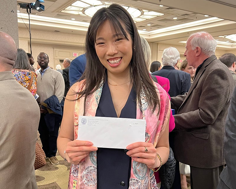 A woman holds her Match Day envelope amid a crowded room