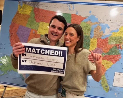 A man and woman embrace near a map of the United States as the man holds a Match Day sign