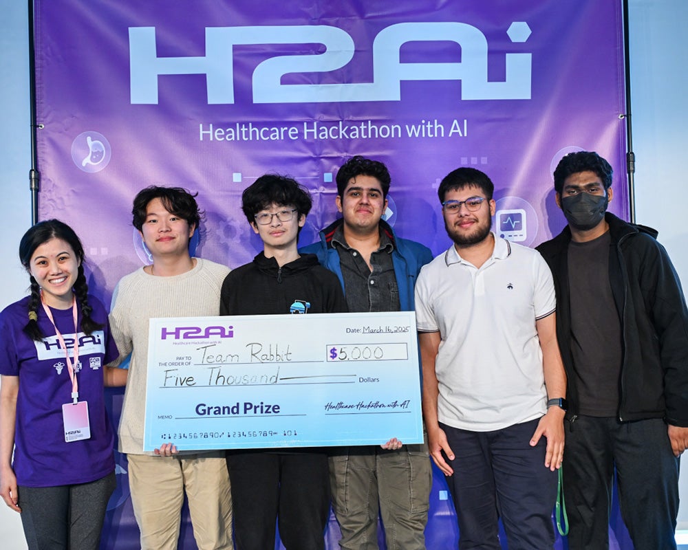 The winning team members stand together and hold a large check representing their $5,000 prize