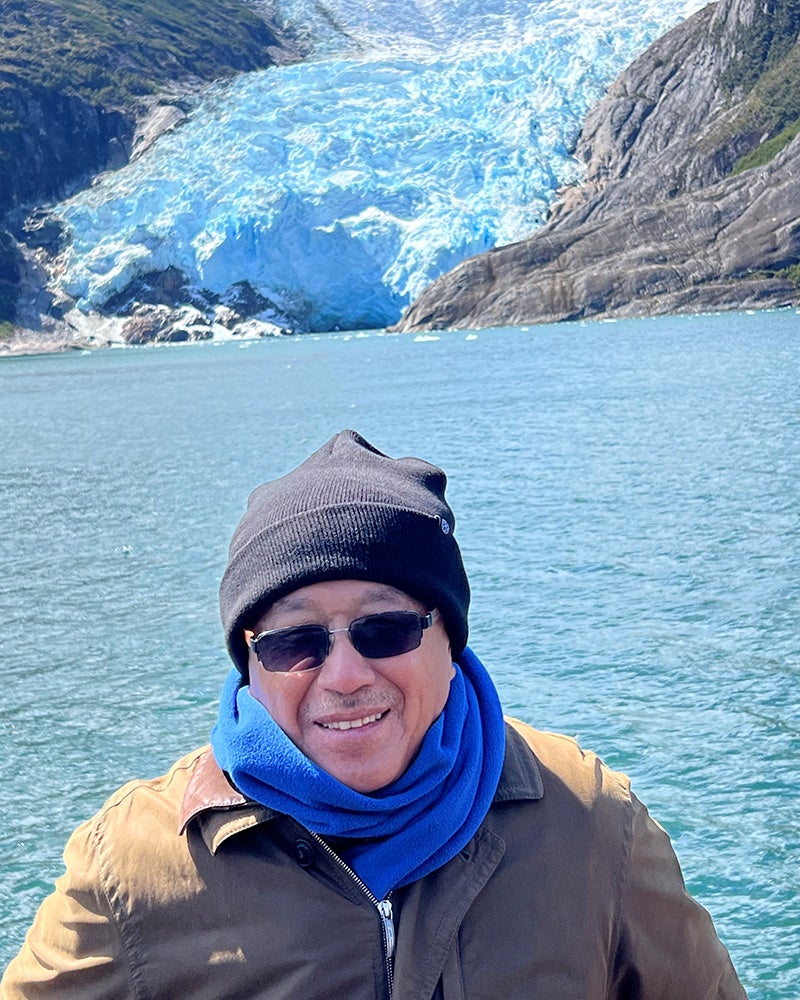 Dr. Dzau in winter gear and sunglasses poses before a lake and glacier