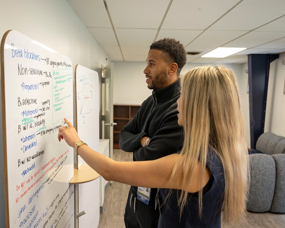 A woman and man look at text written on a whiteboard mounted to a wall in a study space in the annex