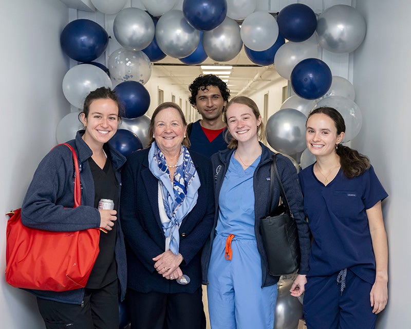 Students stand with Joan Ferrill in a hallway decorated with blue, silver and gray balloons
