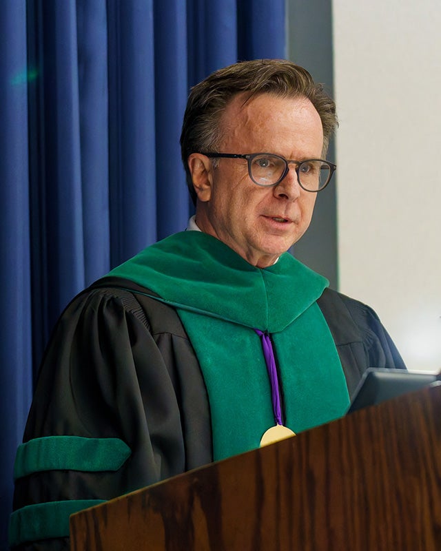 Norman Beauchamp in academic regalia speaks from a podium