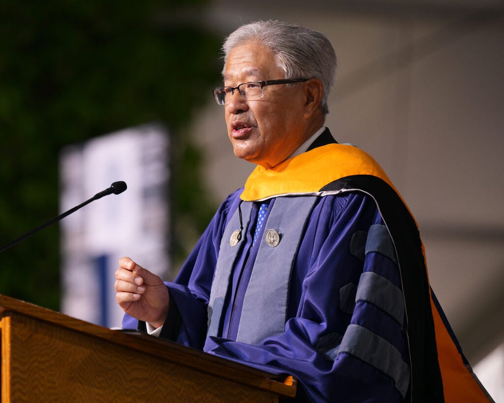 Victor Dzau, dressed in academic regalia, speaks from a podium