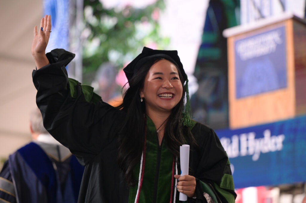 A female student raises her hand as she walks with her diploma onstage