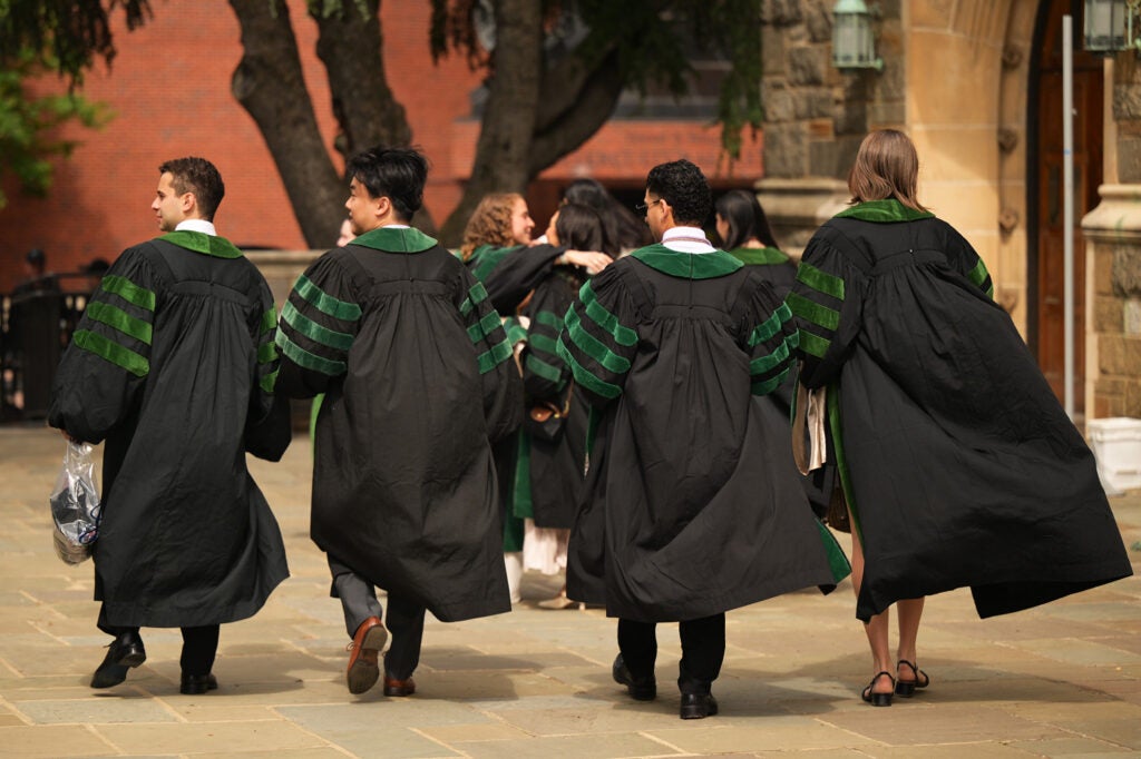 Four students walk outside as the wind billows their academic gowns