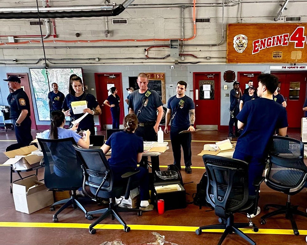 Students check firefighters in at a table surrounded by chairs