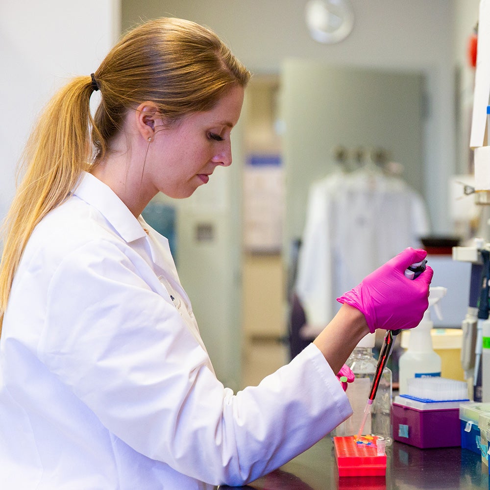 A woman works at a lab bench using a pipette