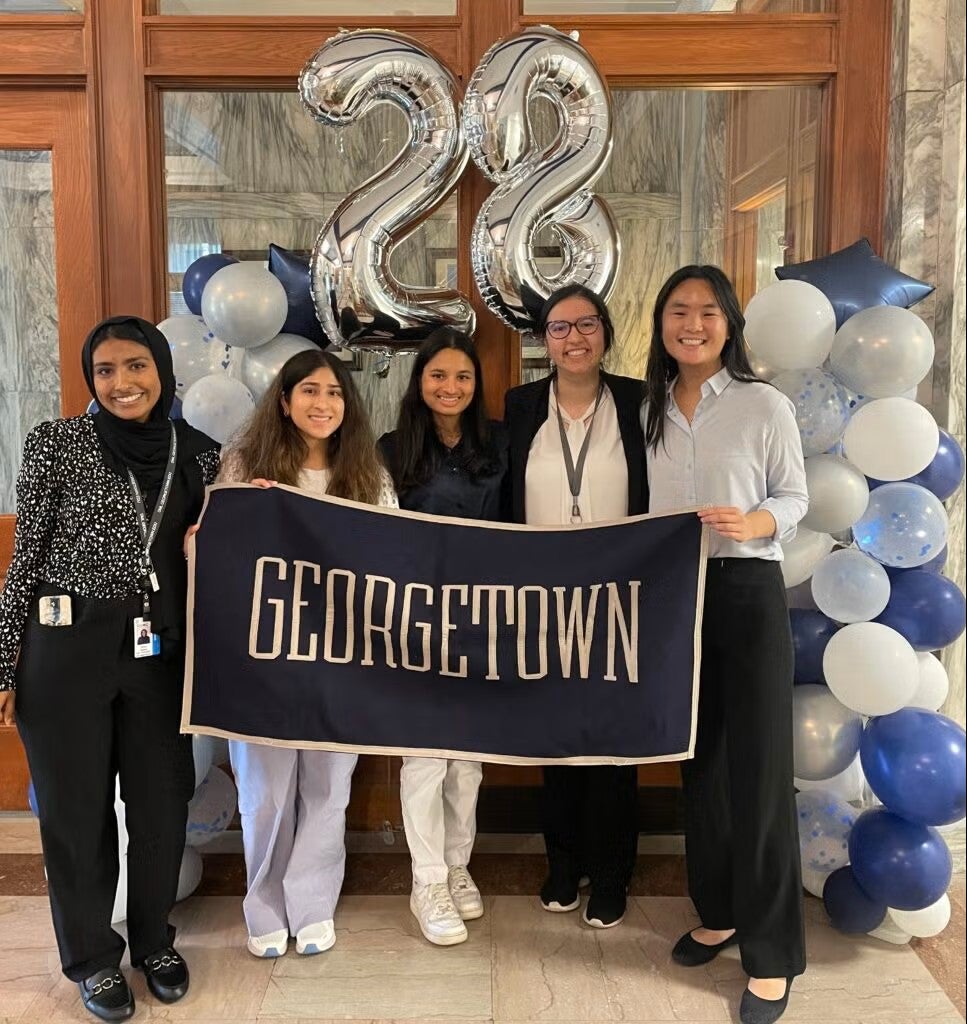 Students stand together with a banner that says Georgetown and balloons behind them including two shaped the the number 28
