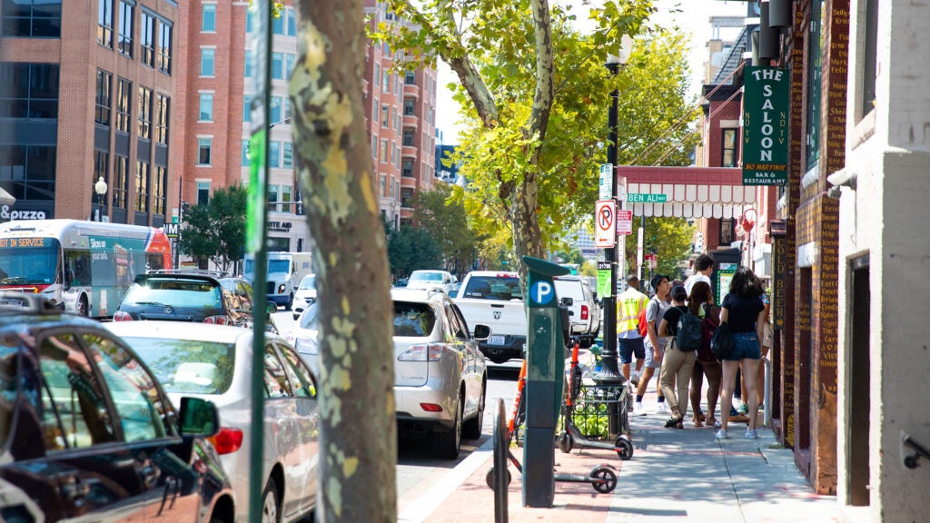 Student walk in a bustling DC neighborhood lined with cars