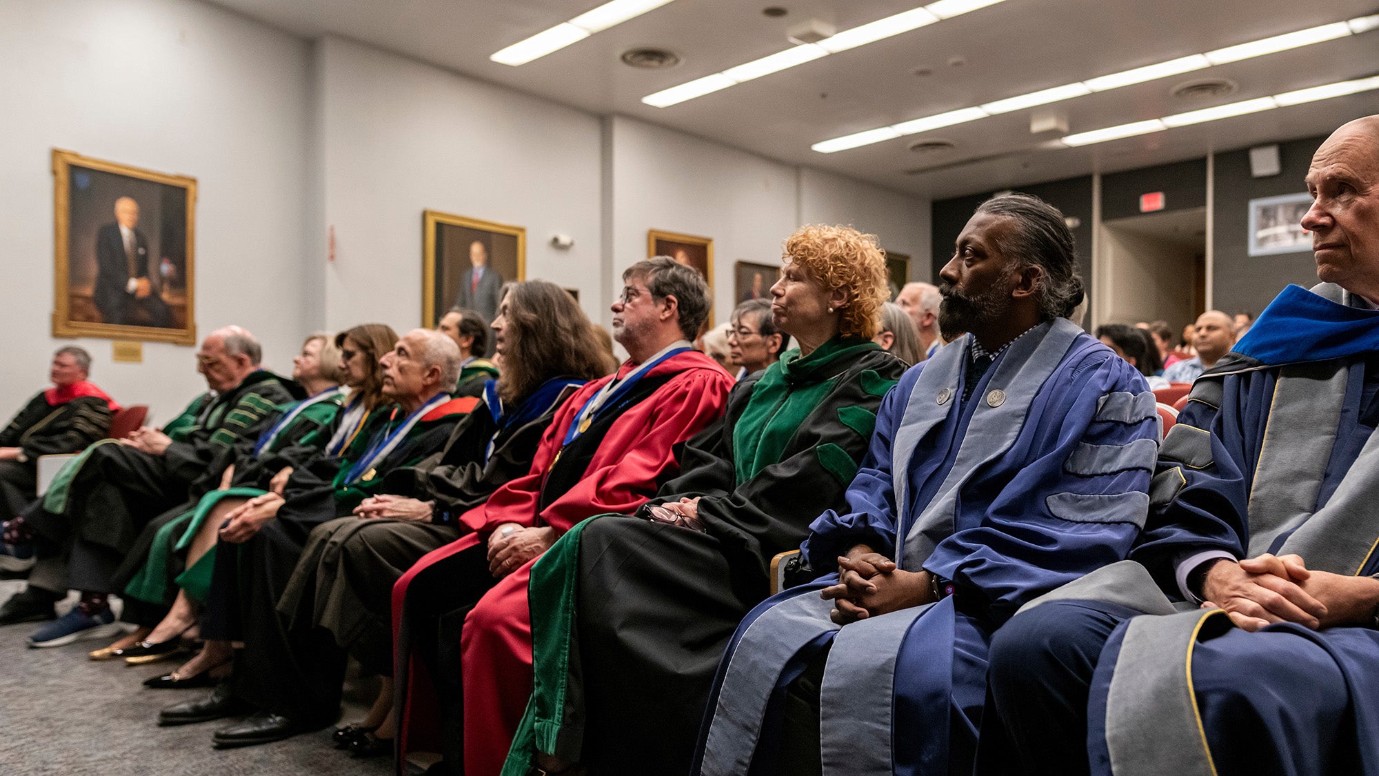 Faculty dressed in academic regalia sit in a row at the MAGIS ceremony
