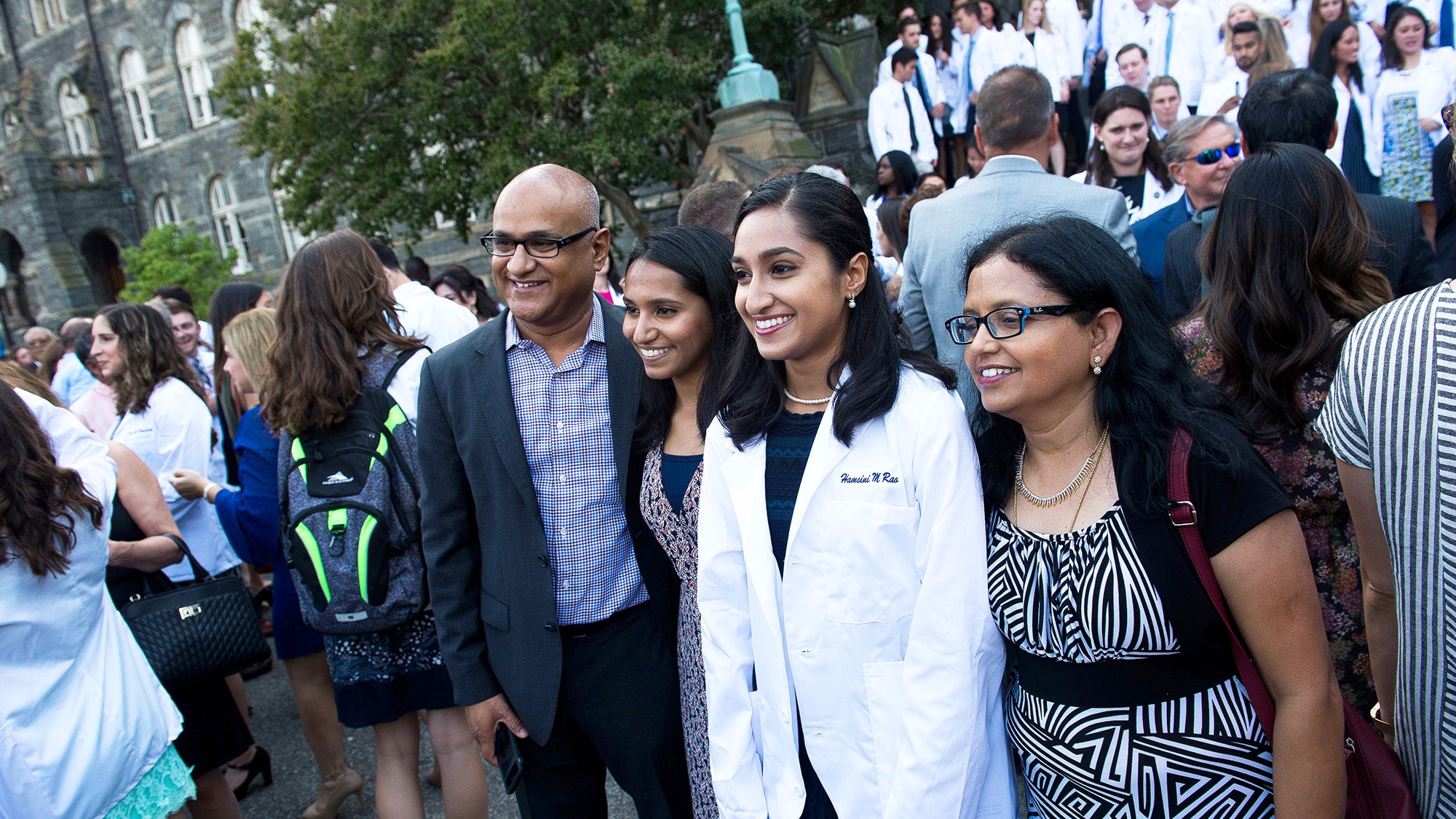 A family with their med student stand for a picture on the steps of Healy Hall while other students and parents mill around them