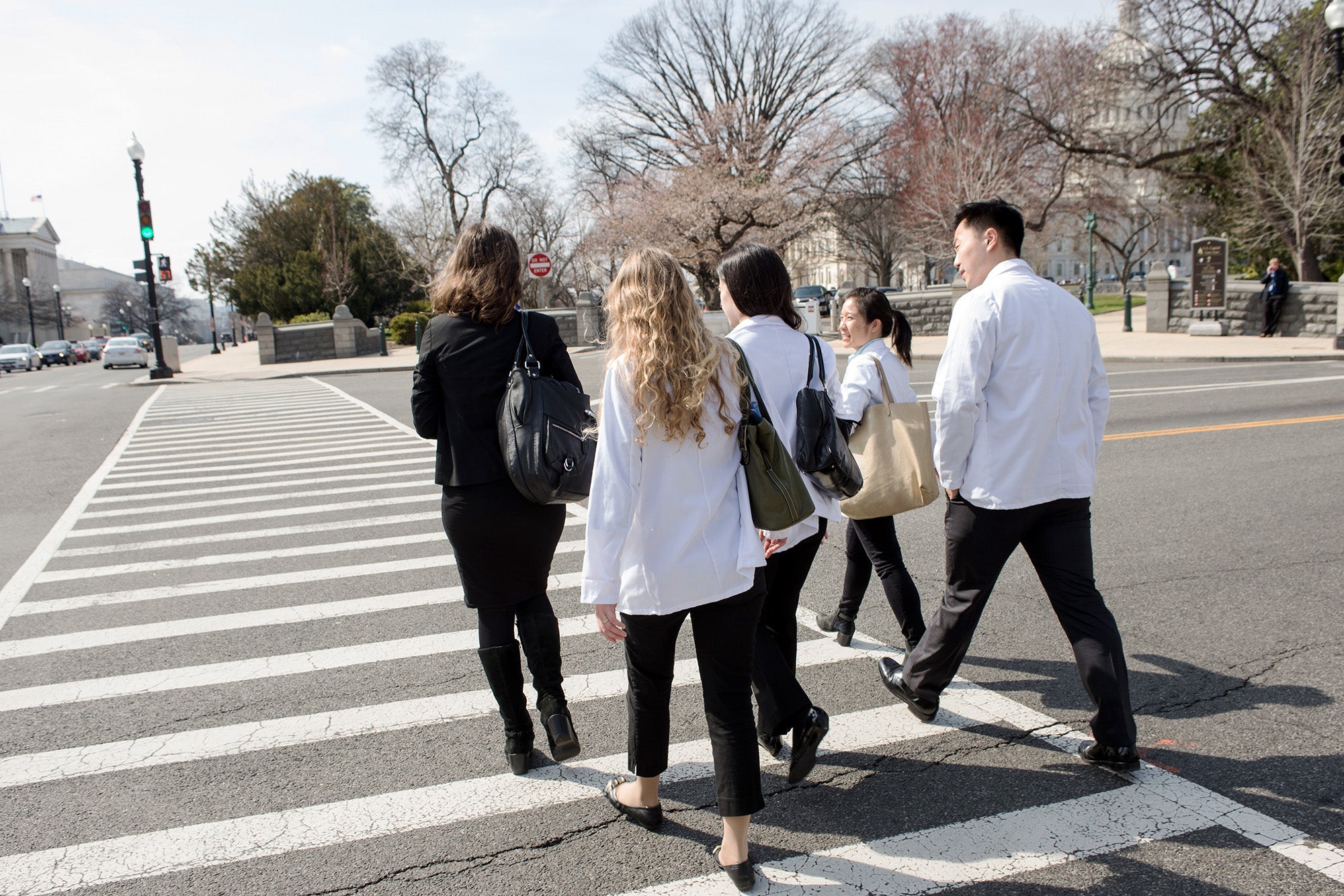 Med students in white coats cross the street near Capitol Hill