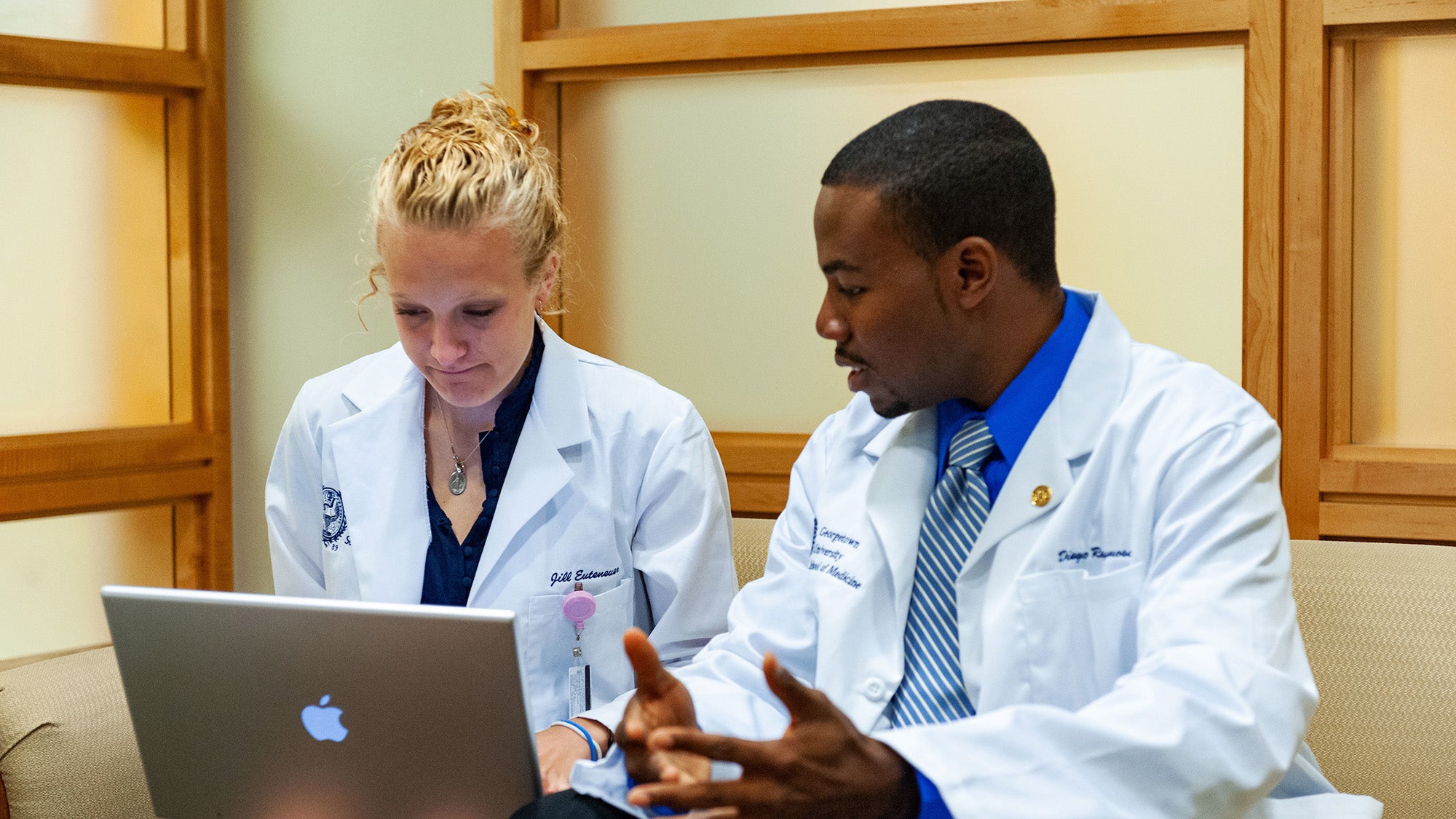 Two students converse as they look at a laptop