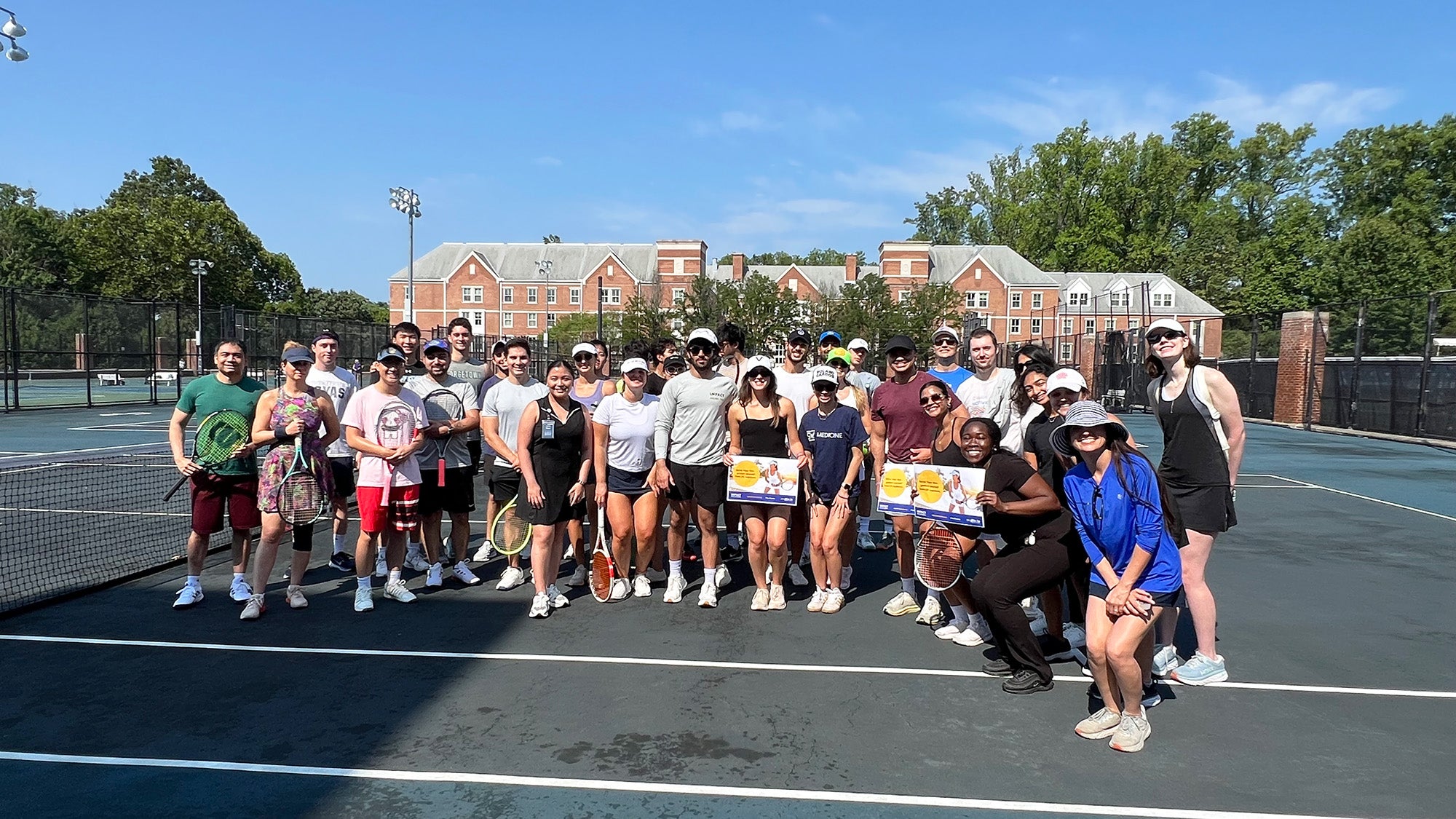 A group of students and faculty stand together on a tennis court