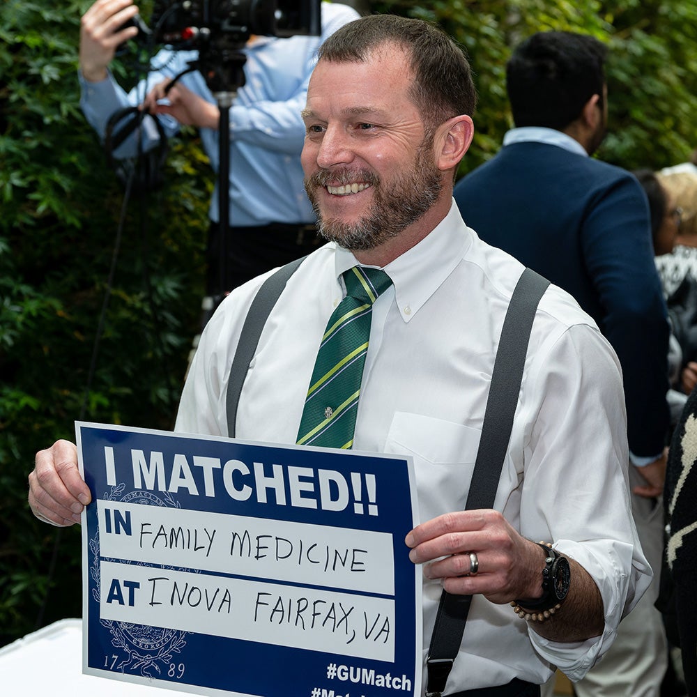A student holds a sign reading I Matched in Primary Care at Inova