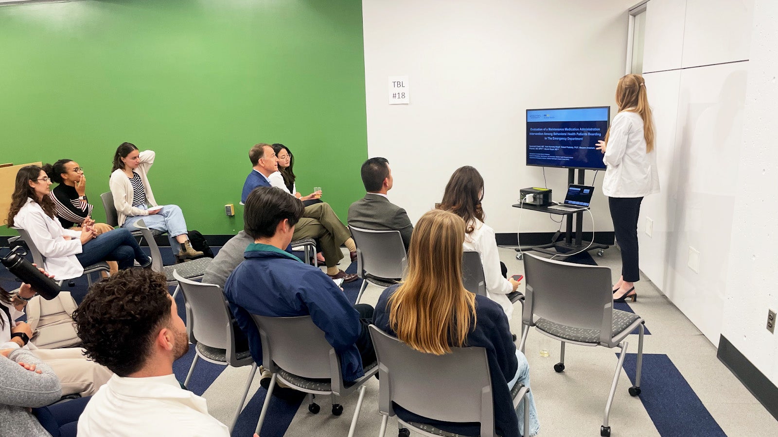 A female medical student gives a presentation before an audience seated in chairs
