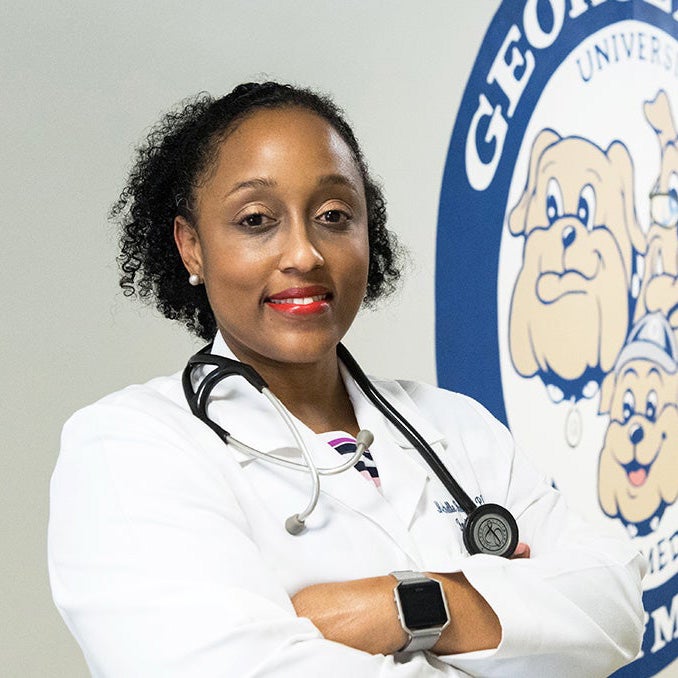 Dr. Michelle Roett stands in a hallway at GUSOM next to a mural of the Department of Family Medicine logo