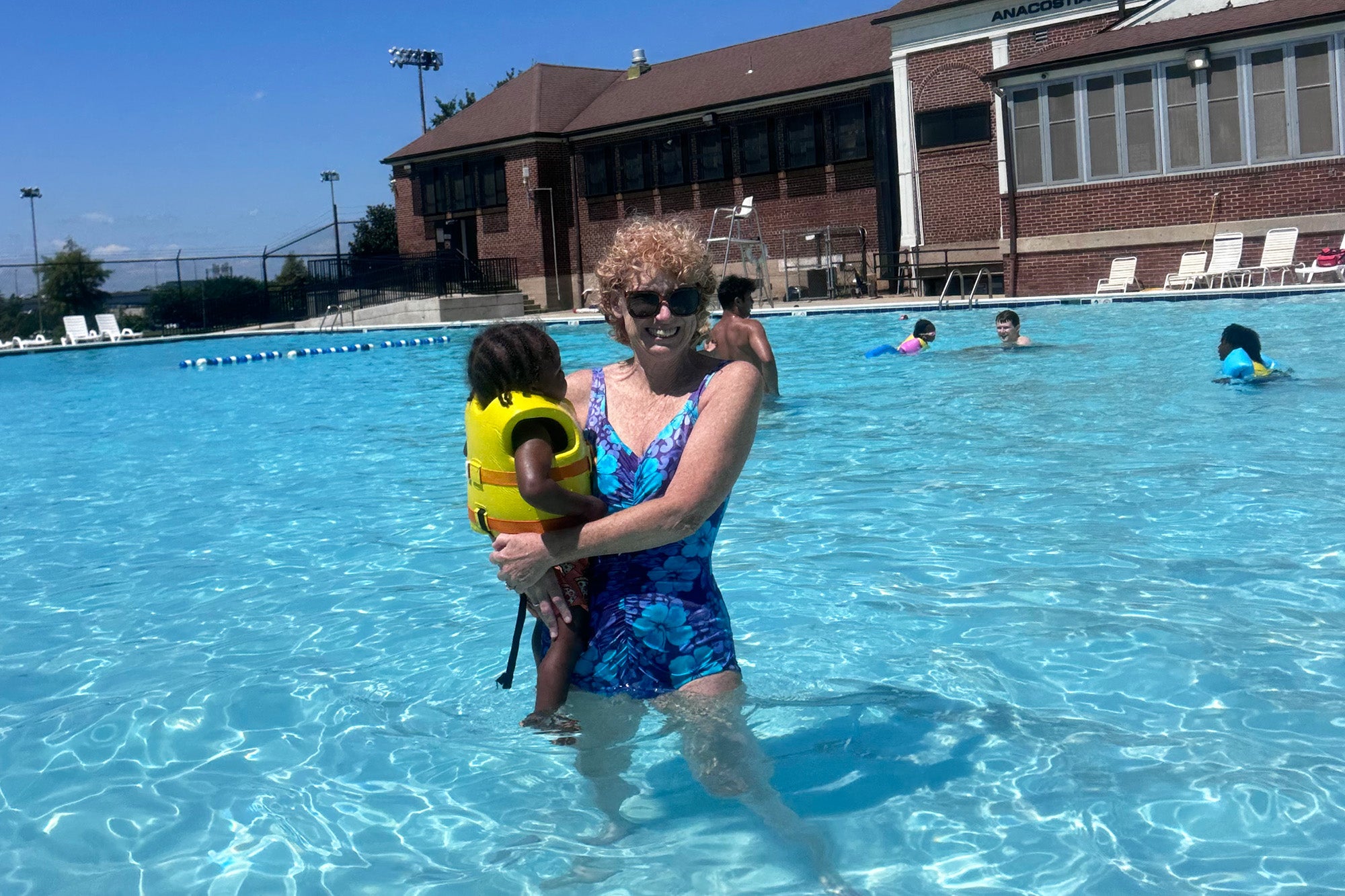 Dr. Moore stands in a large swimming pool holding a small child who is wearing a lifejacket