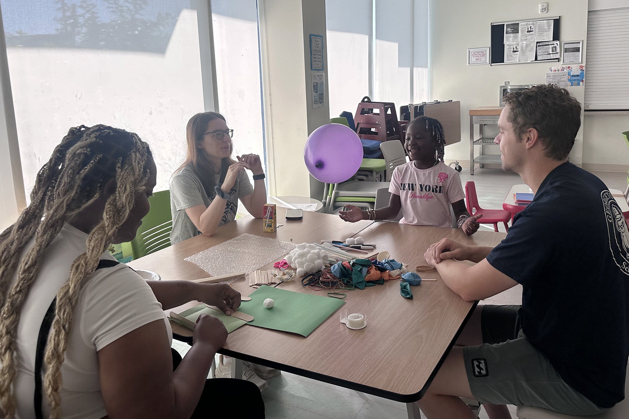 Two medical students and two campers sit at a table making an egg-drop craft with balloons and other craft materials