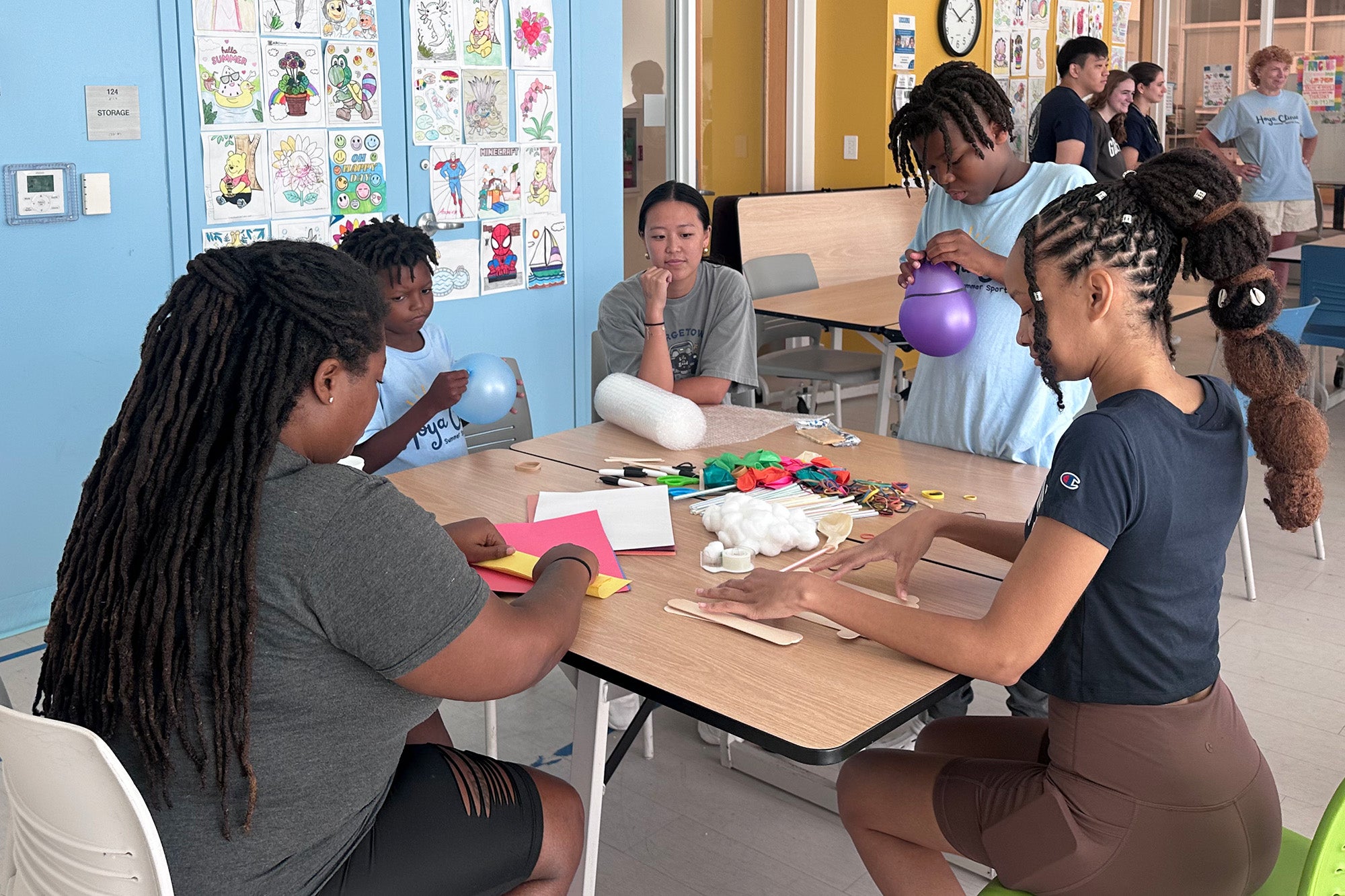 Youth and med students are seated around a table doing a craft activity