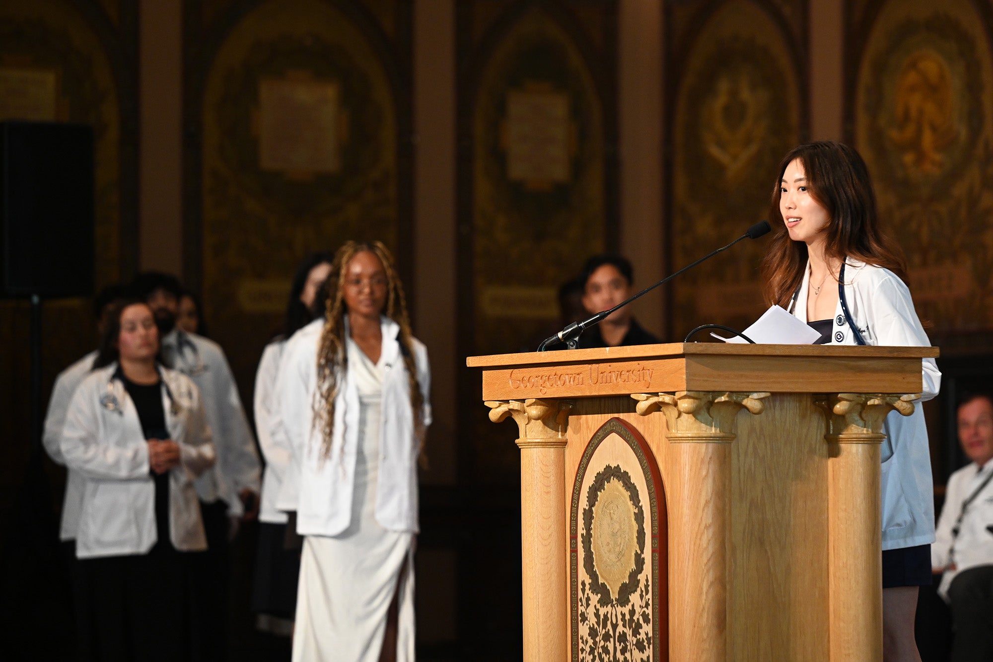 A student speaks from a podium while others wait their turn in the background
