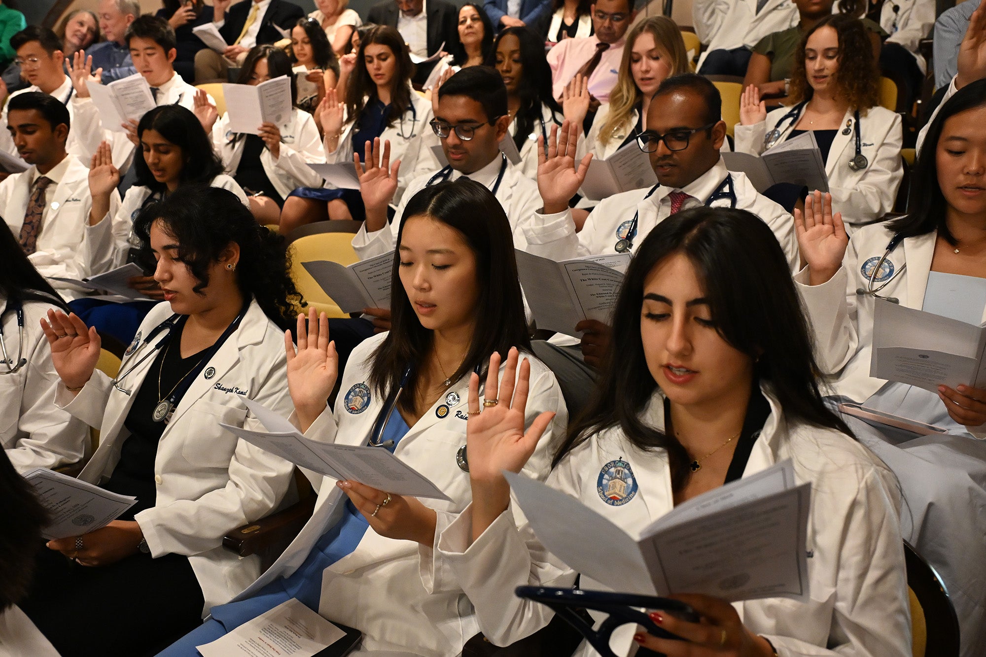 students raise their hands as they read the Hippocratic Oath during the White Coat Ceremony