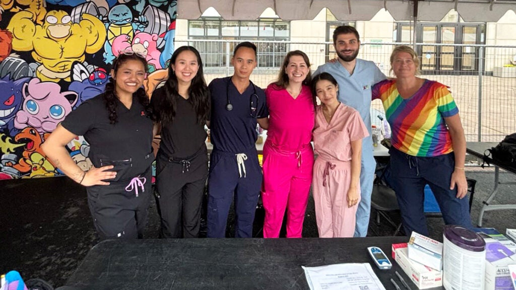 A group of students and faculty stand together in a tent at WorldPride