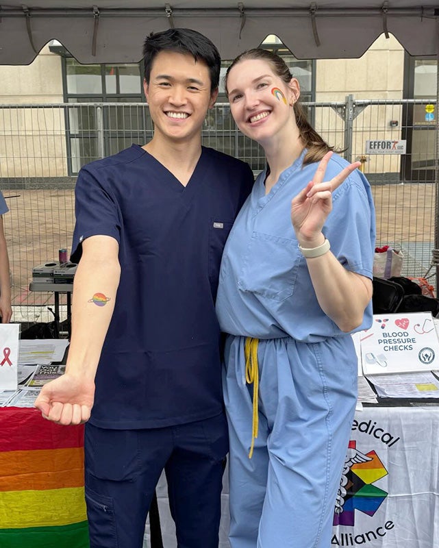 Two medical students stand together in front of the HOYA Clinic tent at WorldPride