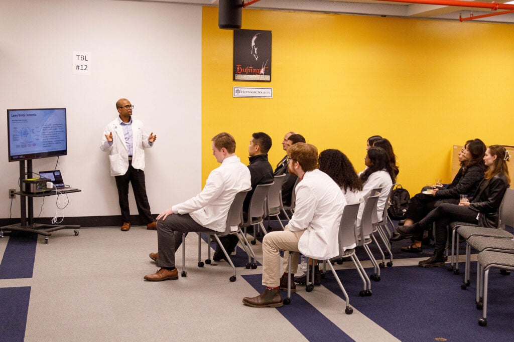 A male medical student gives his presentation to an audience of medical students and others seated in chairs