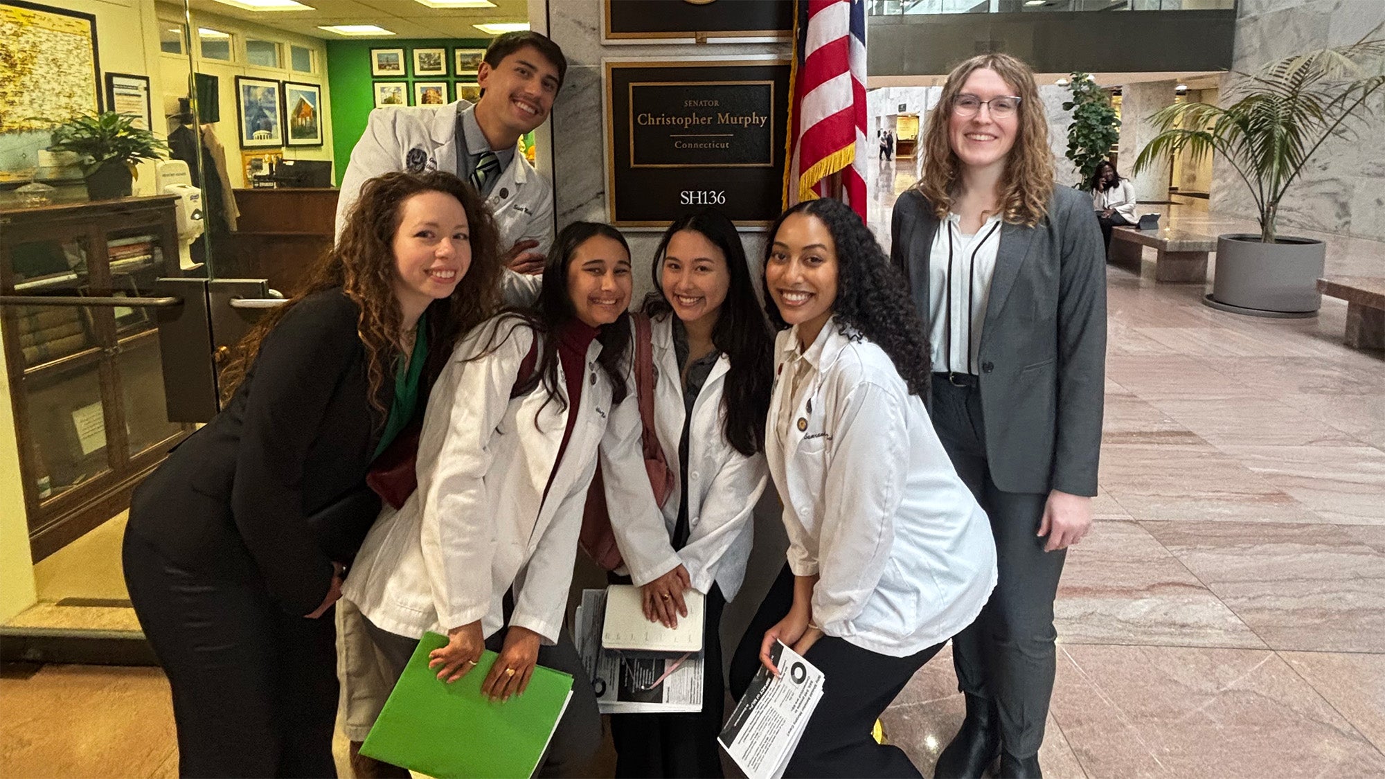 A group of medical and law students stand together for a photo with the sign outside a congressional office