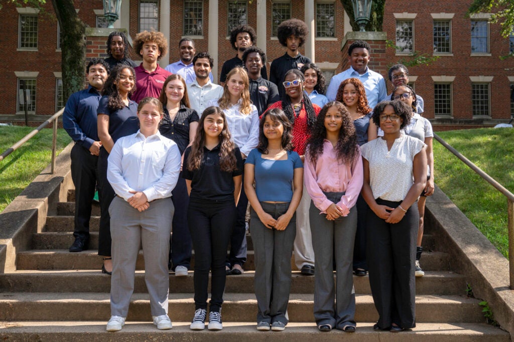 A group of students and mentors stand together on the steps in front of the Med-Dent Building on campus
