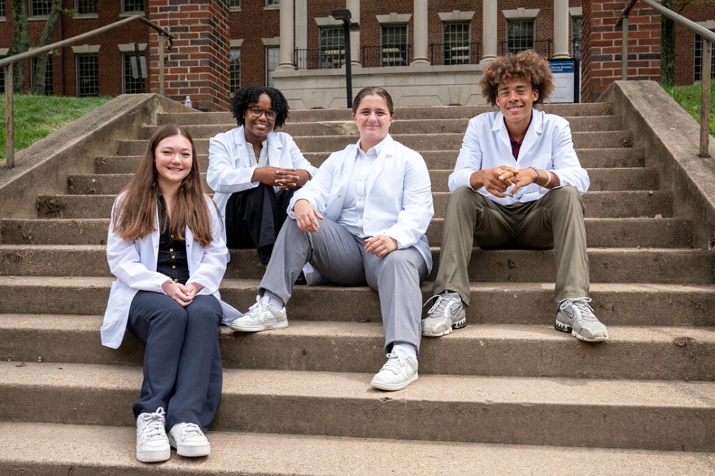 Four students sit on steps in front of the Med-Dent Building on campus