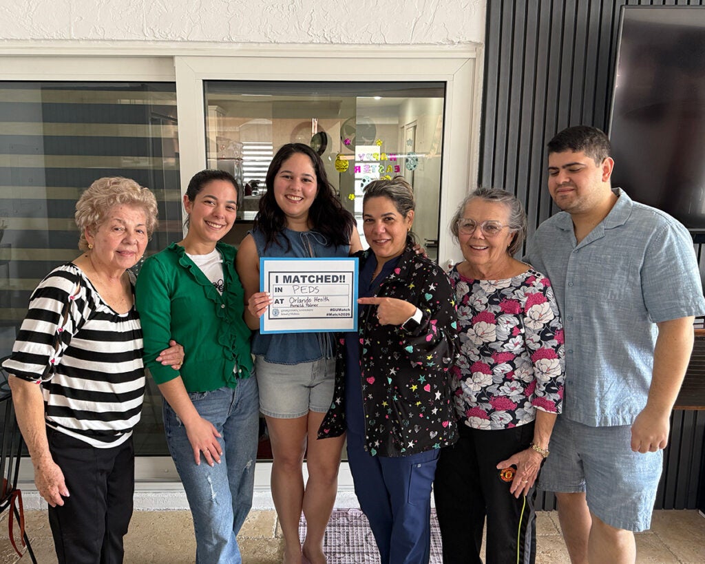 Six individuals stand together, one pointing to a Match Day poster