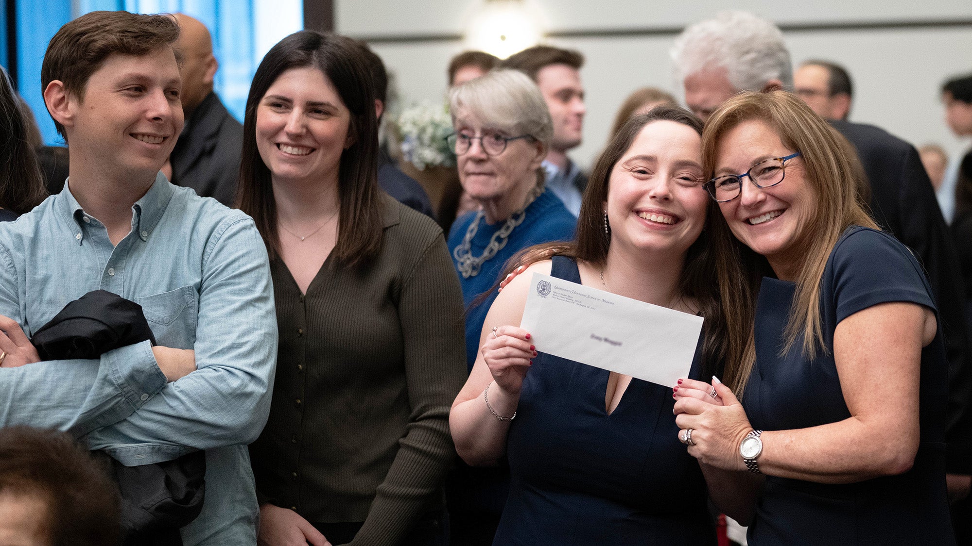 A medical student holds her envelope while embraced by her parent