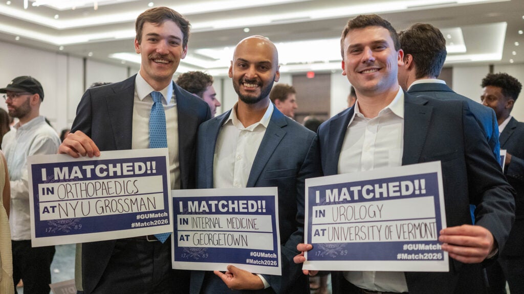 Three male students stand with posters indicating where they matched