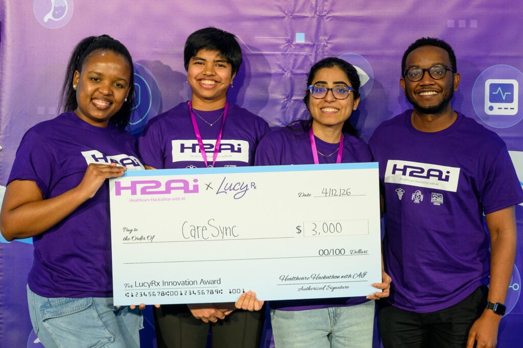 Four individuals stand together with three holding a large award