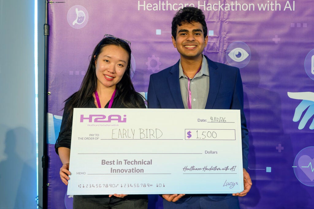 Two individuals stand together holding their large award
