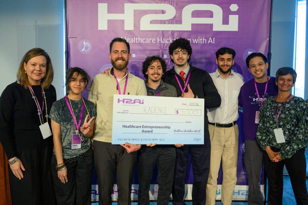 Eight individuals stand together with three holding a large award